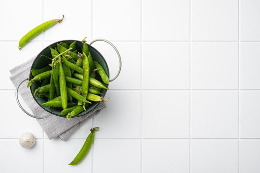 Raw Green Organic Snow Peas, on white ceramic squared tile table background, top view flat lay, with copy space for text