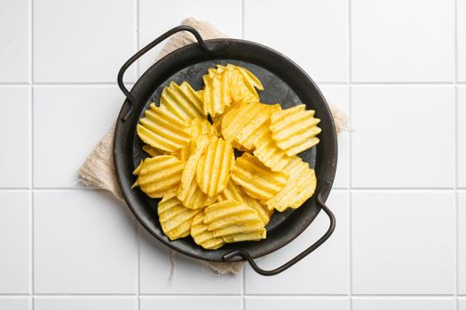 Wavy Salt Pepper Flavored Potato Chips, on white ceramic squared tile table background, top view flat lay, with copy space for text