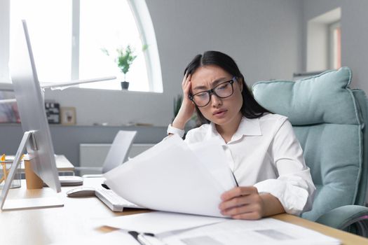 Asian business woman behind paper work, tired and frustrated, working in office, female employee in bra looking at documents and financial reports.