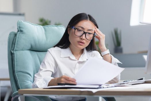 Asian business woman behind paper work, tired and frustrated, working in office, female employee in bra looking at documents and financial reports.