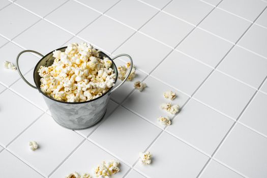 Tasty salted popcorn, on white ceramic squared tile table background, with copy space for text