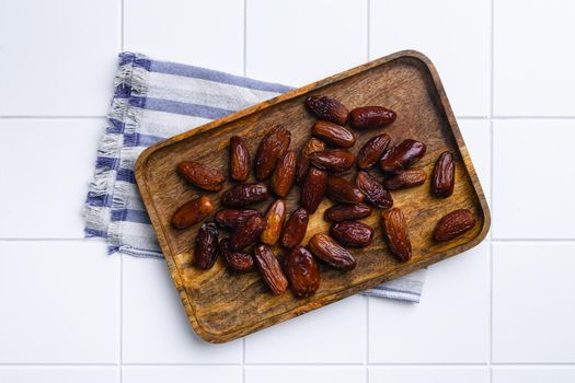 Traditional arabic dry dates, on white ceramic squared tile table background, top view flat lay