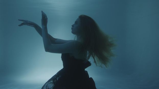 Woman with red hair posing in black dress underwater in 4k