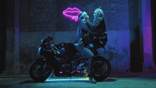 A girl in love and a guy are sitting on a super sport motorcycle flirting and hugging against the background of a neon sign 4k