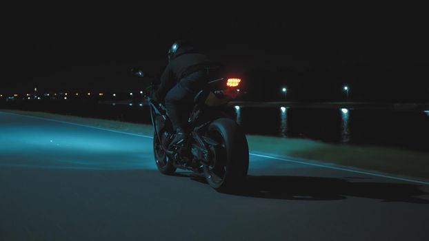 A man rides a sports motorcycle through the city at night against the backdrop of the river in 4k