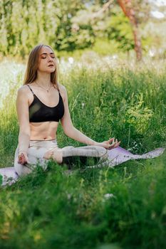 Yoga woman on green grass girl relaxes in the field. Yoga woman in green park girl doing gymnastics outdoors. Meditating woman in meditation in yoga pose practices outdoors