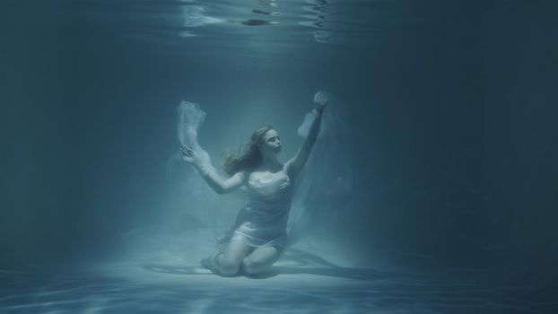 red-haired woman meditating underwater in white dress in 4k