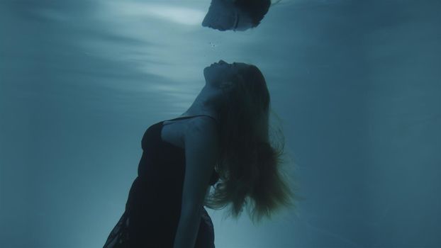 Woman with red hair posing in black dress underwater in 4k