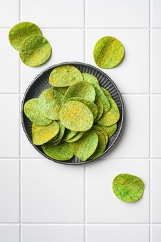Green potato chips, on white ceramic squared tile table background, top view flat lay, with copy space for text