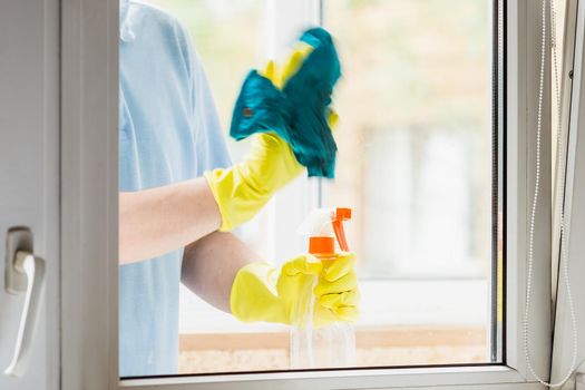 Man in yellow rubber gloves cleaning windows at home. Hand with the rag is blurred by motion