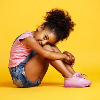 Studio portrait mixed race girl looking sitting alone isolated against a yellow background. Cute hispanic child posing inside. Happy and cute kid smiling and looking carefree in casual clothes.