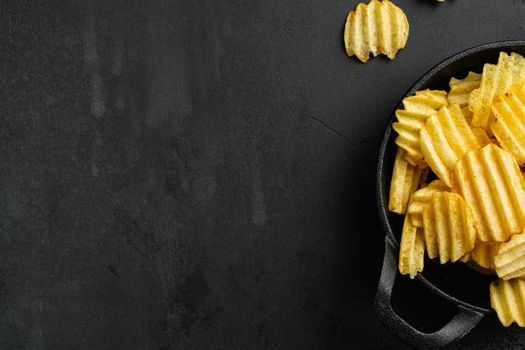 Ridged potato chips, on black dark stone table background, top view flat lay, with copy space for text