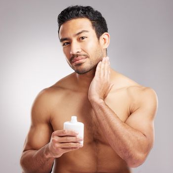 Handsome young mixed race man shirtless in studio isolated against a grey background. Hispanic male applying aftershave after shaving. Take care of your skin when you groom or shave your beard and face.