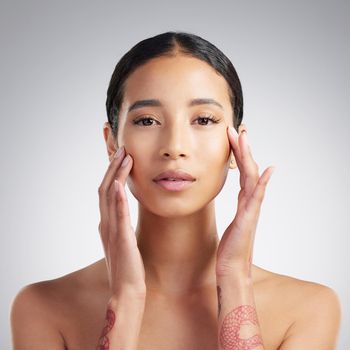 Portrait of a beautiful mixed race woman touching smooth soft skin in a studio. Hispanic model with healthy natural glowing skin looking confident against grey copyspace while doing routine skincare.