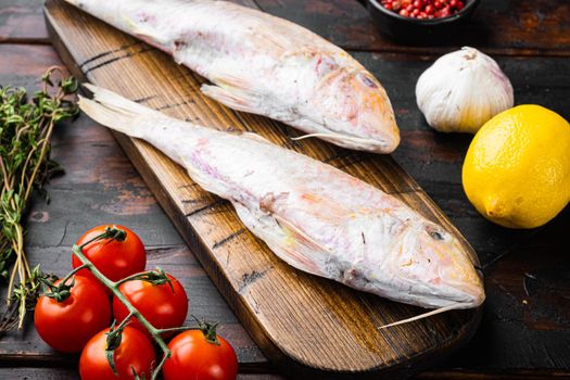 Raw fresh mullet or barabulka whole fish set, with ingredients and herbs, on old dark wooden table background
