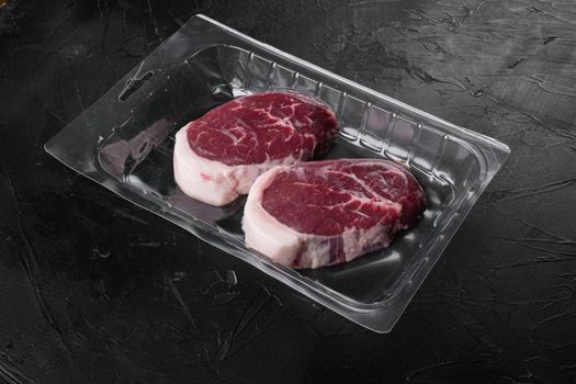 Raw beef steak in vacuum package set, on black dark stone table background, with copy space for text