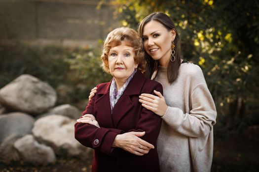 Beautiful adult metis daughter hugs caucasian mom in park in autumn outdoors. High quality photo