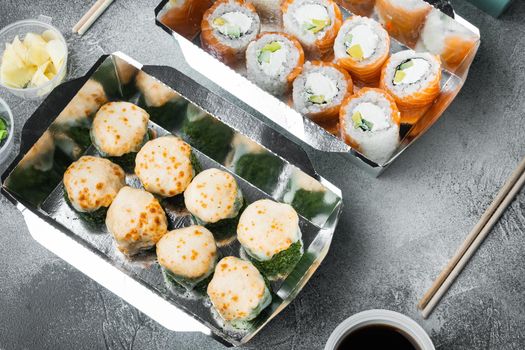 Tasty sushi rolls in disposable boxes set, on gray stone background