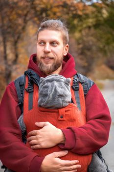 Young smiling babywearing father with his baby in baby sling fall outdoor adventure.