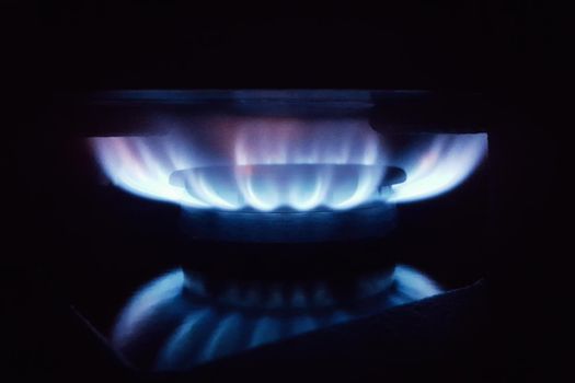 Blue flame of household gas on a kitchen stove on a black background.