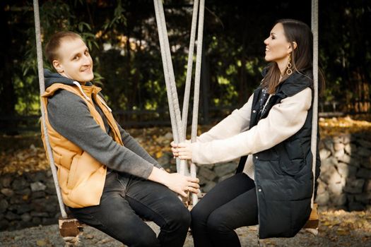 Young couple on a date sits on a swing in the forest among the trees. High quality photo