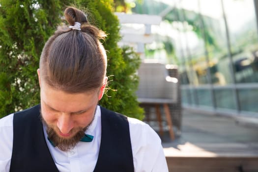 Hipster hairstyle on a young bearded man in a suit sitting in a street cafe.