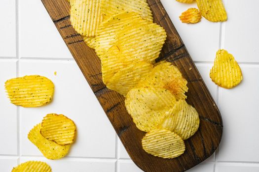 Golden corrugated potato chips, on white ceramic squared tile table background, top view flat lay