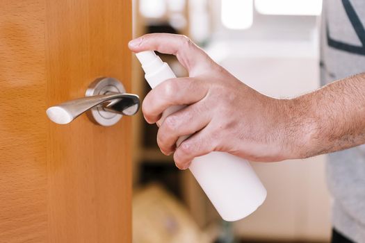 hand of a man sanitizing a doorknob with disinfectant spray, hygiene concept and protection against viruses and bacteria