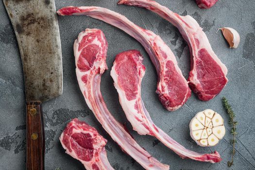 Raw fresh lamb loin chops set, with ingredients carrot orange, herbs, and old butcher cleaver knife, on gray stone background, top view flat lay