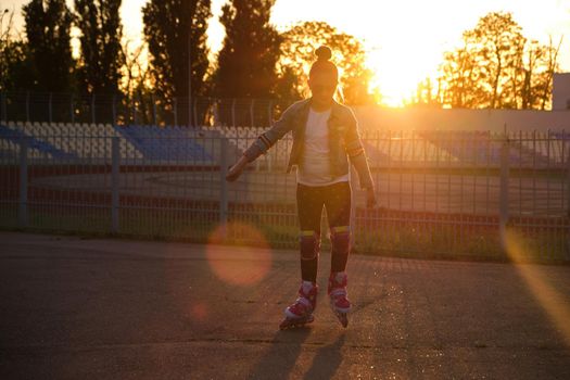 Little pretty happy funny girl on roller skates at stadium at sunset, learning to roller skate outdoors. Outdoor activity for children. Active sport for preschool kid. sun glare, selective focus