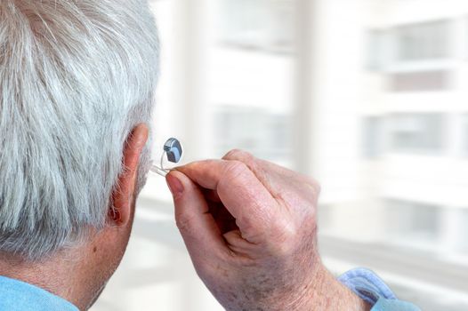 American plan on the installation of a hearing aid of a senior with white cheuveux rear view.