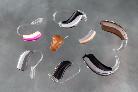 Presentation of a wide range of hearing aids seen from above on a gray background.