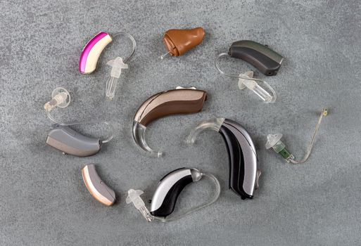 Predentation of a wide range of hearing aids seen from above on a gray background.