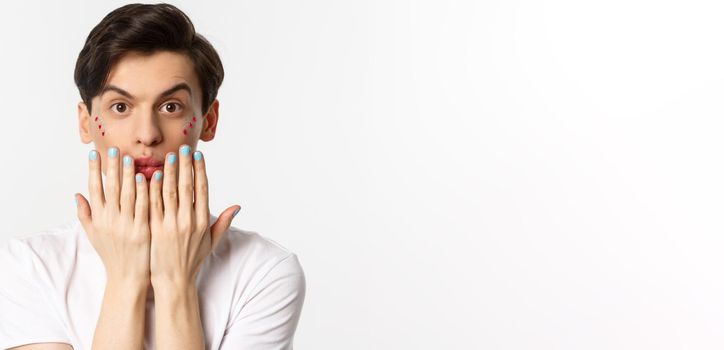 People, lgbtq and beauty concept. Beautiful gay man showing blue nail polish on fingernails and looking at camera, have manicure, standing over white background.