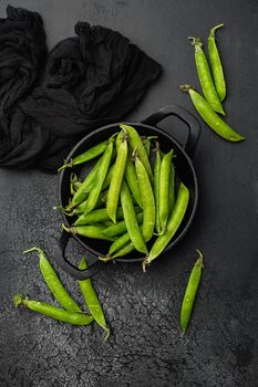 Green pea pod, on black dark stone table background, top view flat lay