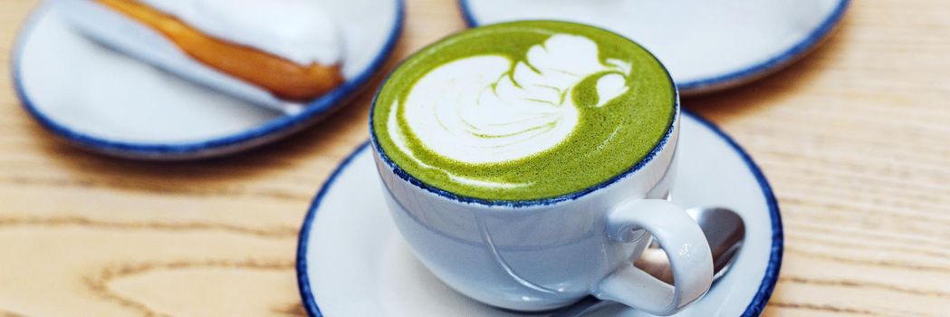 Blue and green matcha in glasses on a wooden table in a coffee shop next to a sweet dessert. Web banner.