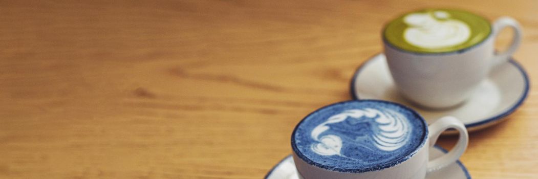 Blue and green matcha in ceramic white mugs on a wooden table with copyspace. Web banner