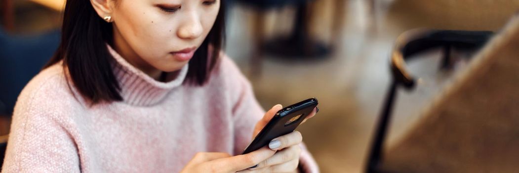 Asian lovely girl climb on the phone in a coffee shop. A pretty beautiful woman is looking for information on the Internet or working. Web banner.