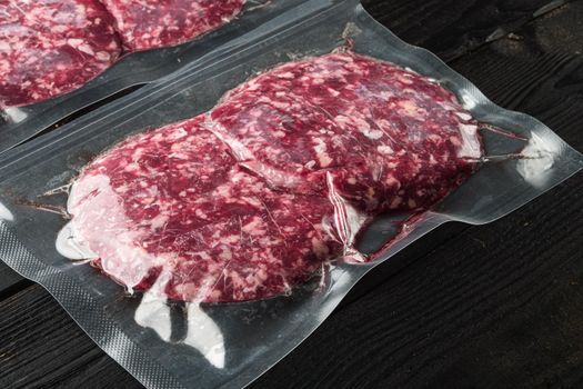 Burger beef veal cutlets in vacuum plastic set, on black wooden table background