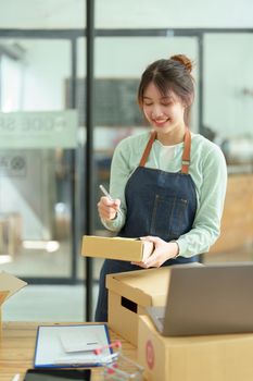 A portrait of a small startup, and SME owner, an Asian female entrepreneur, is writing down information on a notepad to organize the product before packing it into the inner box for the customer.