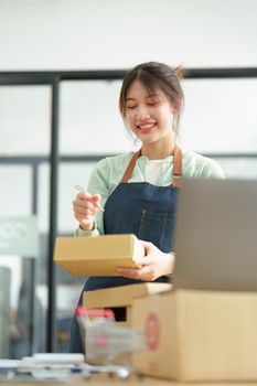 A portrait of a small startup, and SME owner, an Asian female entrepreneur, is writing down information on a notepad to organize the product before packing it into the inner box for the customer.