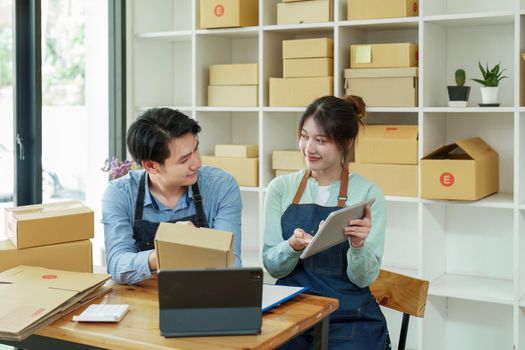 Portrait of a small start-up and SME owner, an Asian male and female entrepreneur checking orders and packing for customers, self-employed, freelance, online selling.