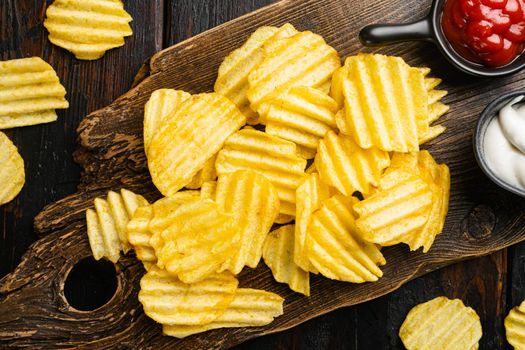 Golden corrugated potato chips, on old dark wooden table background, top view flat lay