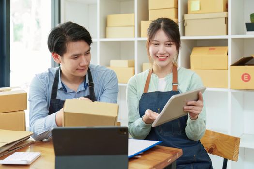 Portrait of a small start-up and SME owner, an Asian male and female entrepreneur checking orders and packing for customers, self-employed, freelance, online selling.