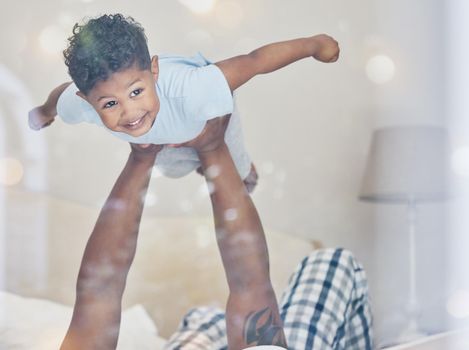 Happy little mixed race boy flying in fathers arms looking at camera in bedroom. Dad holding and lifting cute little child playing and having fun on bed.