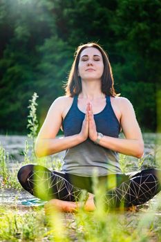 a woman practices yoga and meditates in the lotus position on the sand against the backdrop of trees, soft focus