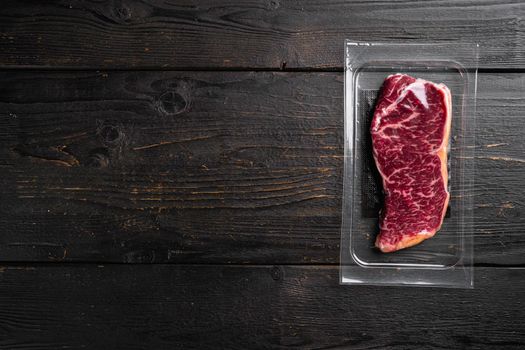 Raw Striploin marbled beef steak vacuum Packed set, on black wooden table background, top view flat lay, with copy space for text