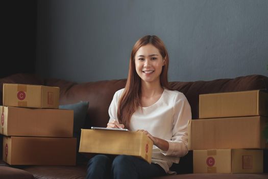 Image of Young asian woman startup freelance with parcel box and talking with customer by computer laptop. Online marketing packing box delivery concept