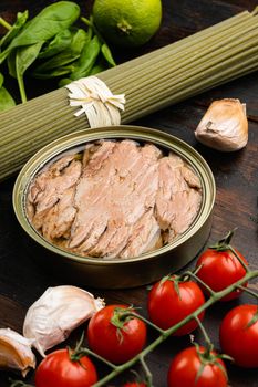 Smoked canned tuna in cooking oil in open tin can set, on old dark wooden table background