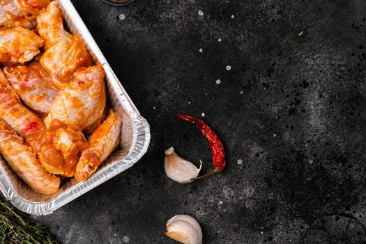 Marinated chicken wings in red sauce set, on black dark stone table background, top view flat lay, with copy space for text